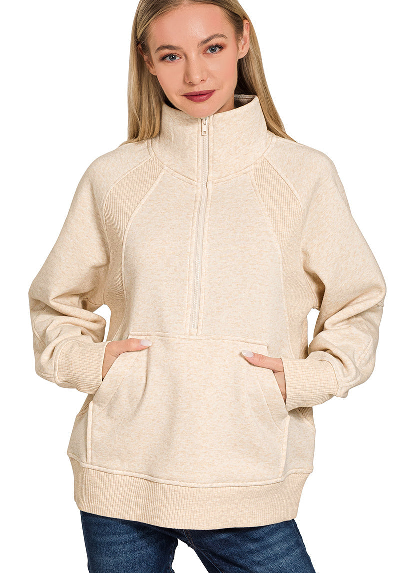 Woman wearing a beige zip-up hoodie with blue jeans on a white background